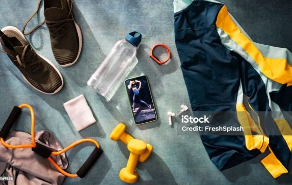 Mobile phone surrounded with various fitness-related objects, clothes, equipment and technology, all in a blue-toned overhead composition.