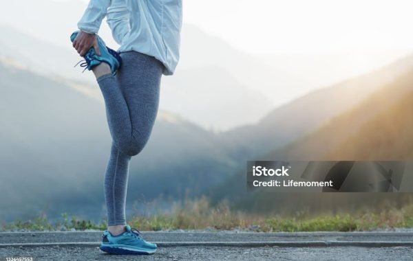 Fit stretch woman stretching quad leg muscle standing getting ready to run jogging outside. Athlete trail running in the mountains on a beautiful morning.