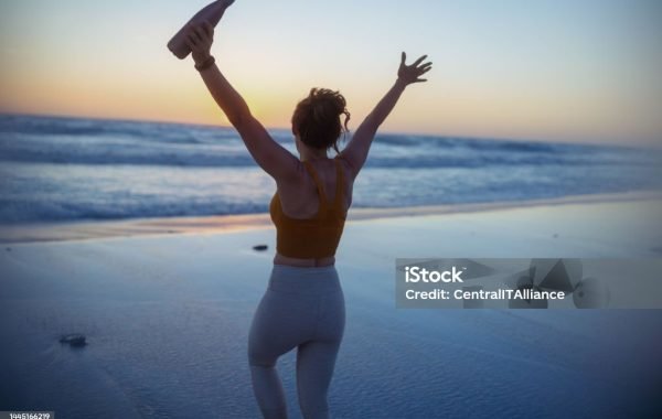 Seen from behind fit woman jogger in sport clothes with bottle of water rejoicing.