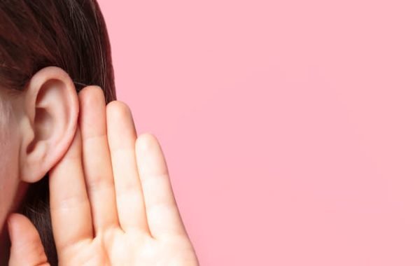 The girl listens attentively with her palm to her ear close-up on a pink background