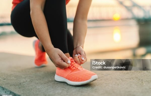 Close up of sporty woman tying shoelace while kneeling outdoor, In background bridge. Fitness outdoors concept.